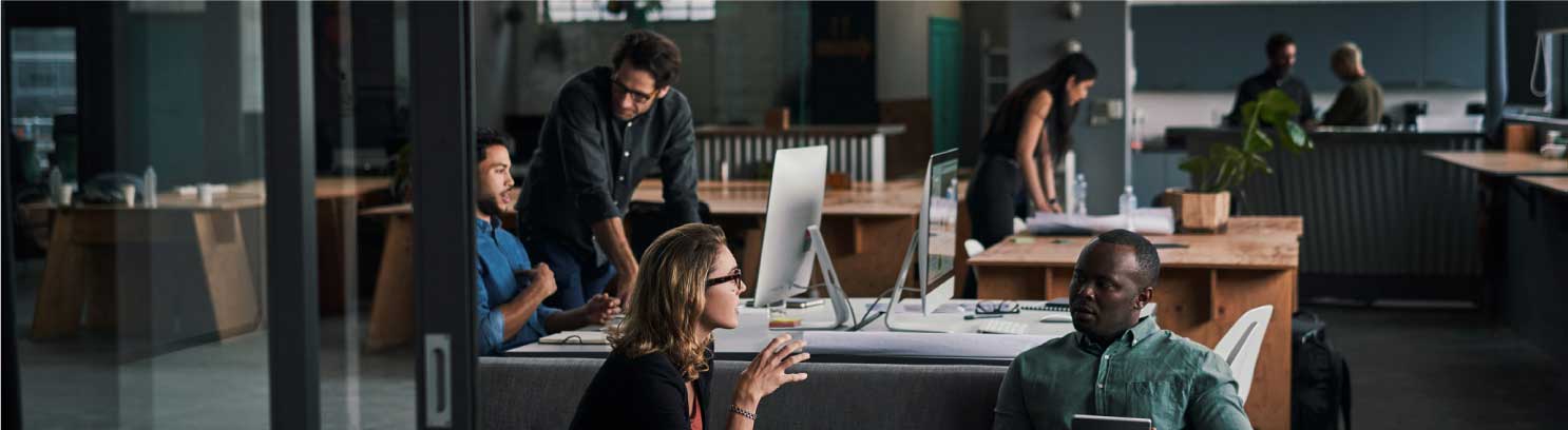 coworkers conversing in office building with desks and computers