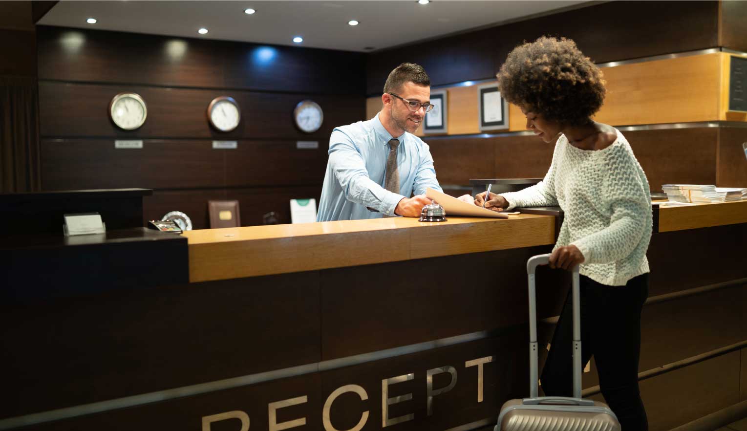 Receptionist at front desk of hospitality establishment handing guest papers to sign