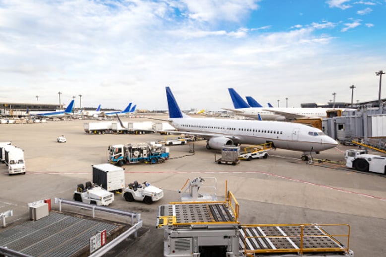 Photo showing a wide view of a jet bridge at the airport filled with parked commercial airplanes, baggage tugs, and ramp-ups